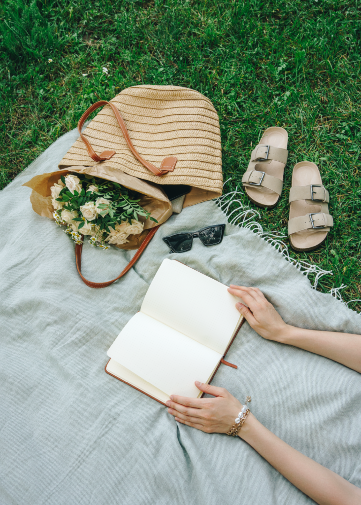 blanket, purse, shoes, sunglasses and book at a park